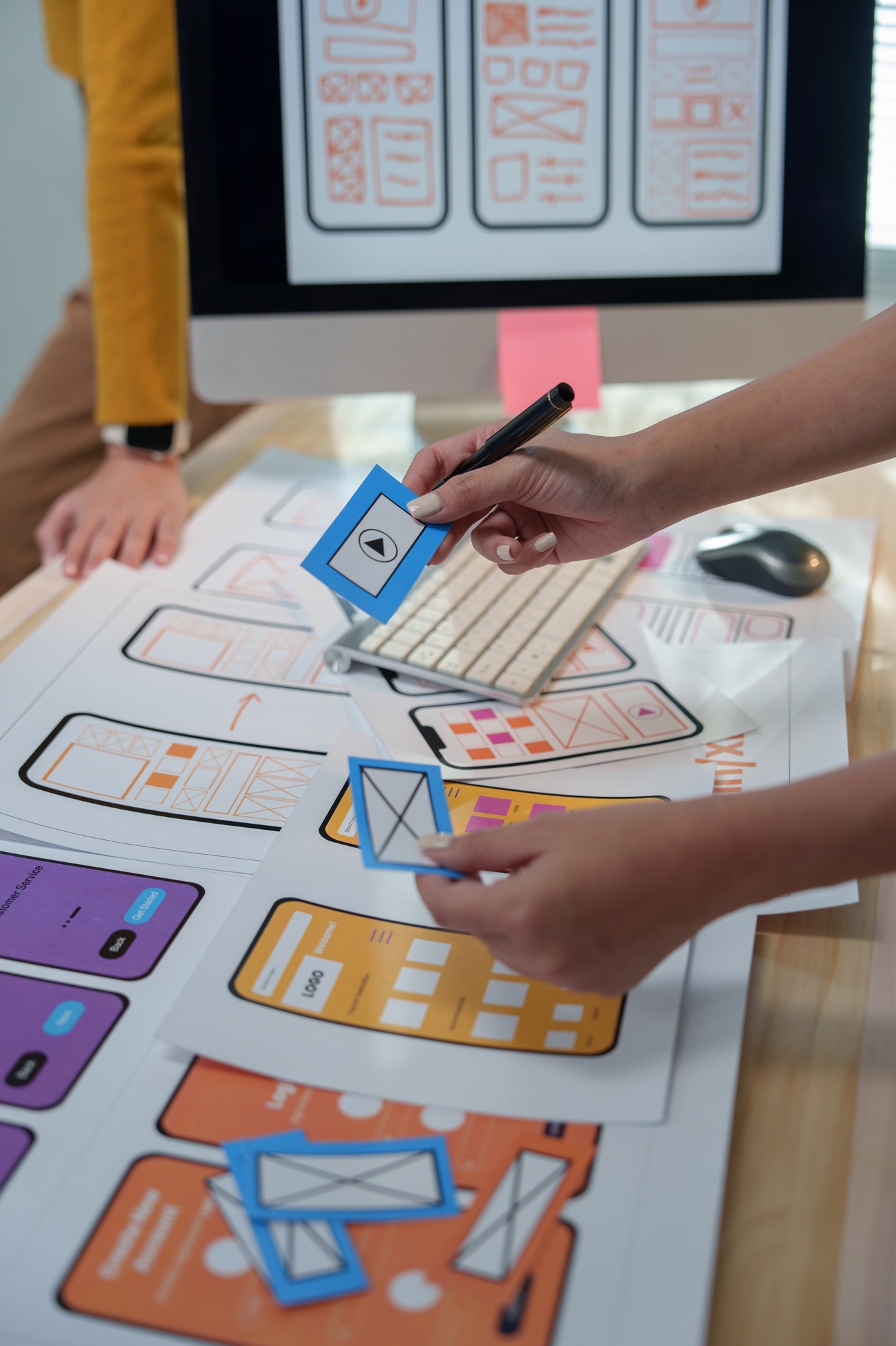 Two ux designers collaborating on wireframing a mobile app, arranging blue cards with icons on print